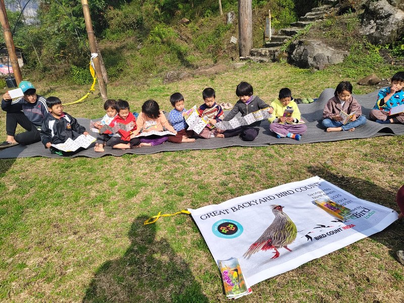 Children sitting outdoors with bird pocket guides during a GBBC session in Sikkim.